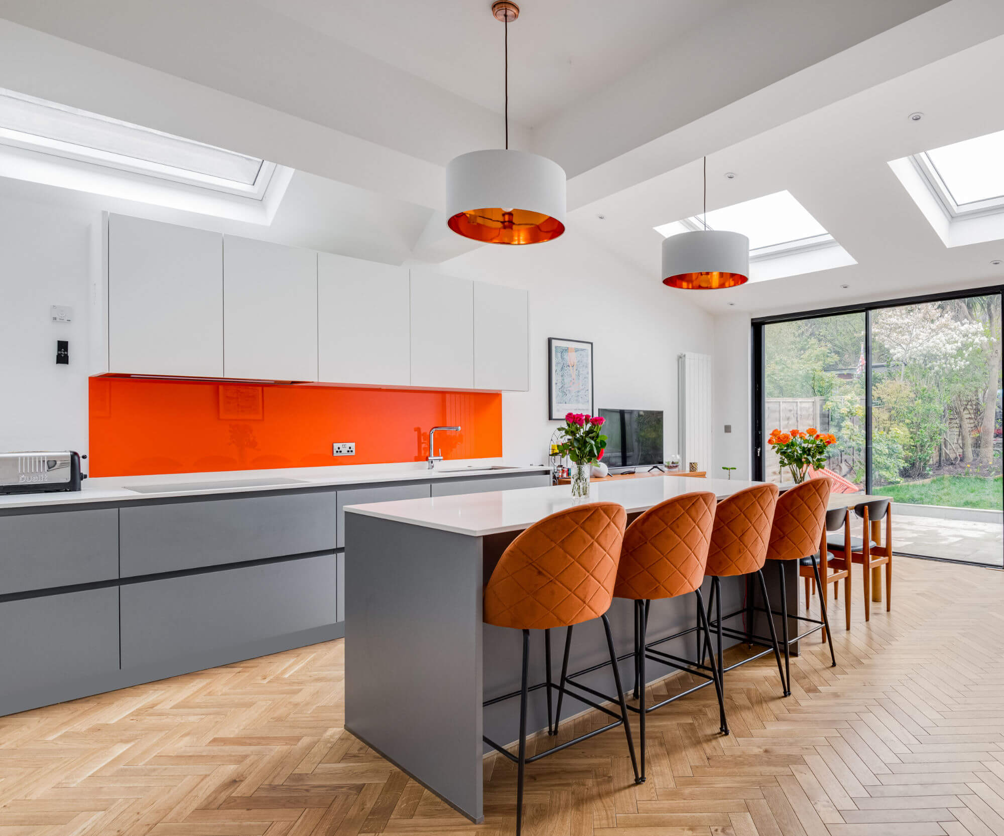 A German kitchen with grey handless kitchen units and an orange glass splash back